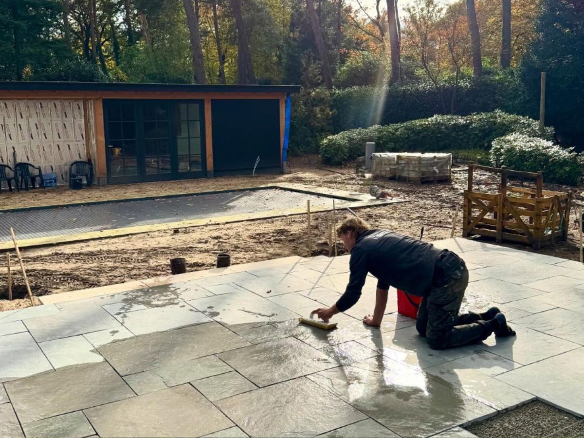 Hovenier werkt aan een groot terras in een tuin in aanleg.